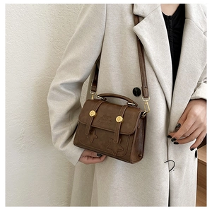 Close-up of brown vintage crossbody bag with star stitching and metallic round buckle