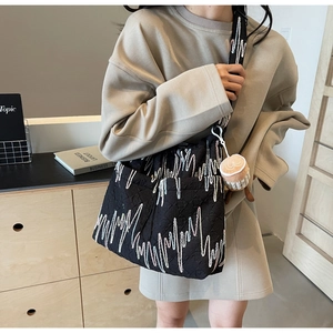 Close-up of black quilted tote bag with heart-wave pattern and coffee cup plush charm