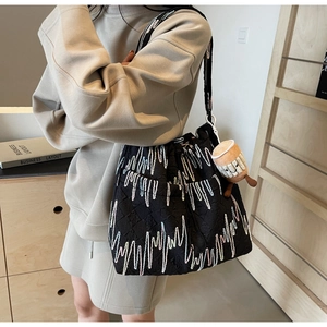 Detail of black quilted tote bag with colorful embroidery and coffee cup plush charm