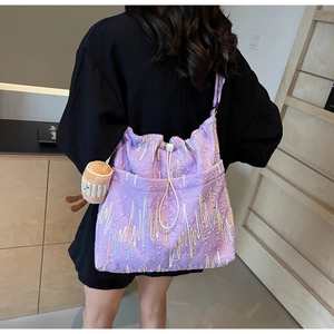 Detail of purple tote bag with rainbow embroidery and plush charm worn by a model