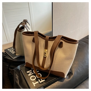 Detail of canvas tote bag with brown leather trim and golden metal lock closure