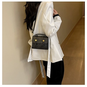 Detail of a black crossbody bag with star-stitched pattern and gold buckles on the flap