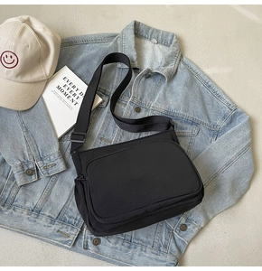 Détail du sac bandoulière en nylon noir avec sangle large près d'une veste en jean