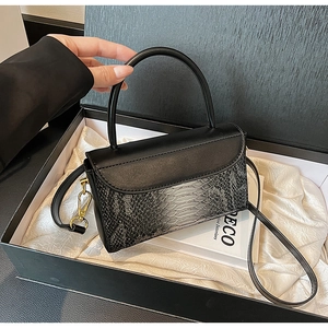 Detail of black crocodile texture bag featuring gold metal hardware and rigid handle