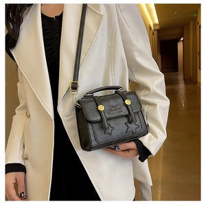 Detail of black leather crossbody bag with star stitching and gold rivets on a white blazer