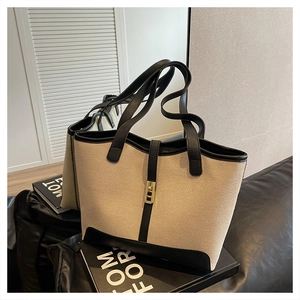 Detail of beige canvas tote bag with black leather trim and elegant golden metal lock