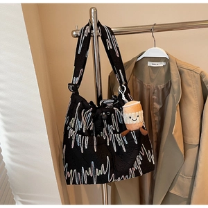 Detail of black quilted tote bag with colorful wave embroidery and plush charm