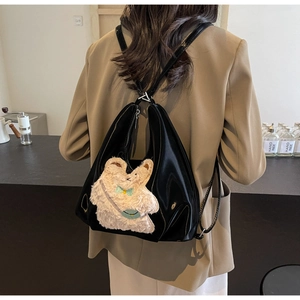 Sac à dos noir brillant avec petit ours en peluche 3D, porté sur une veste beige