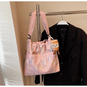 Detail of pink tote bag with wavy embroidery and plush cup accessory on strap