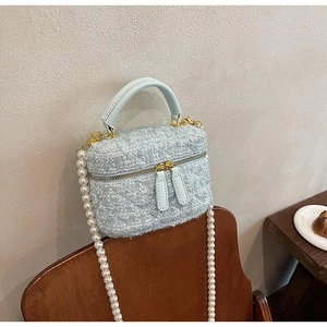 Détail d'un sac seau en tweed bleu clair avec bandoulière en perles et dorures