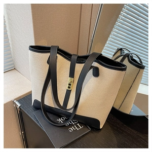 Detail of canvas tote bag with black leather trim, metal buckle, and sturdy shoulder straps