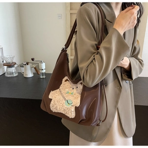 Détail du patch ours en peluche 3D avec nœud vert sur un sac fourre-tout en PU marron