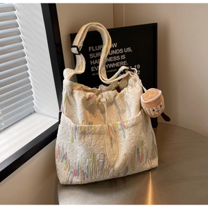 Detail of white textured fabric tote with colorful stripes and plush cup pendant