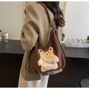 Sac fourre-tout en cuir brun avec broderie d'ours en peluche dans un décor de café