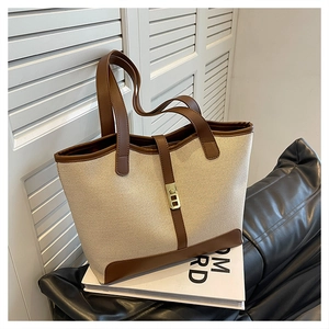 Detailed view of canvas tote bag with brown leather trim and golden metal buckle clasp