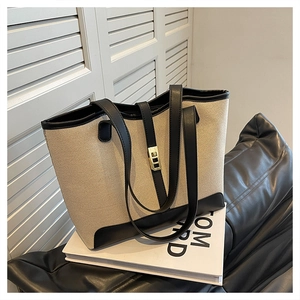 Close-up of beige canvas tote bag with black leather trim and golden twist lock detail