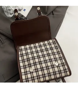 Detailed close-up of brown checkered backpack with metallic magnetic snaps and leather trim