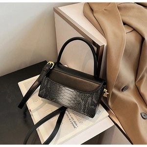 Detail of black crossbody bag with grey faux snake texture and gold metal hardware buckles