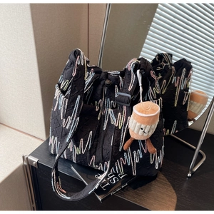 Close-up of black quilted tote bag with colorful wave embroidery and plush cup charm