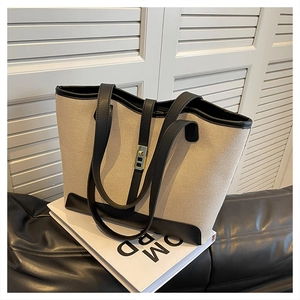 Close-up of minimalist canvas tote bag featuring black leather trim and gold twist lock