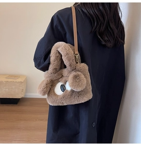 Detailansicht der braunen Plüschtasche mit verspielten Augen-Akzenten und einem Pompon