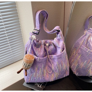 Detail of purple tote bag with quilted texture, side pockets and colorful embroidery