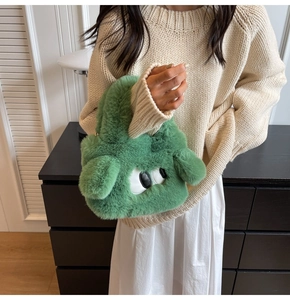 Detailaufnahme einer grünen Plüschtasche mit Augen-Dekor auf einem Strickpullover