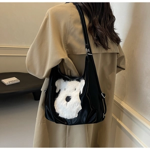 Détail d'un sac cabas en cuir verni noir avec une adorable broderie de chiot en peluche blanche