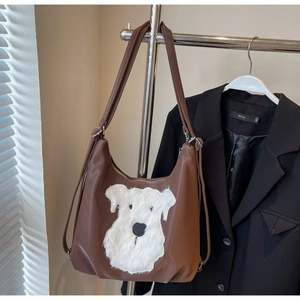 Détail d'un sac hobo en cuir marron avec broderie chiot en peluche blanche et deux anses