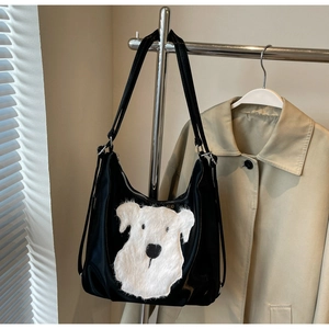 Détail d'un sac cabas en nylon noir avec broderie chiot en peluche blanche sur un cintre