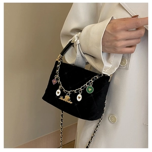 Detail of black velvet quilted handbag featuring colorful charms and metal chain strap