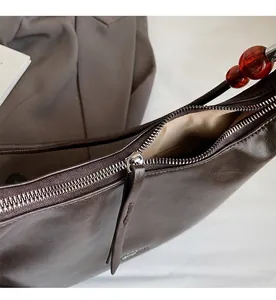 Detail view of smooth silver zipper and amber bead on dark brown leather shoulder bag