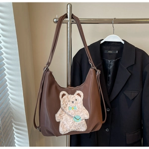 Détail d'un sac cabas marron avec un patch ours en peluche et des bretelles réglables