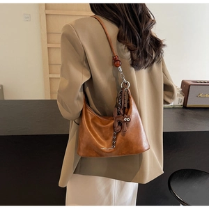 Detail of a brown leather crescent shoulder bag with a beaded strap and cat charm