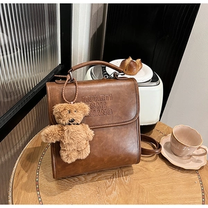 Dettaglio ravvicinato dello zaino vintage in pelle marrone con goffratura e orsetto