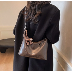 Detail of dark brown leather shoulder bag featuring a cute cat charm and tassel accent