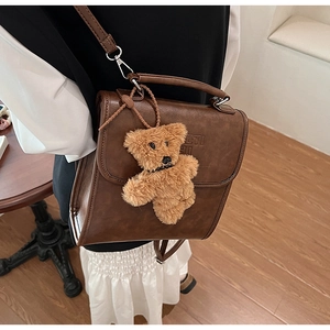 Dettaglio borsa vintage in pelle marrone con lettere a rilievo e ciondolo a forma di orso