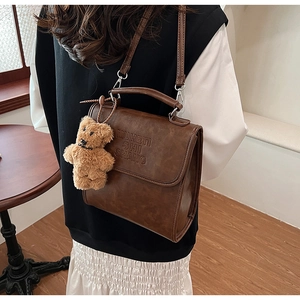 Dettaglio della borsa vintage in pelle marrone con lettere goffrate e ciondolo a orsetto