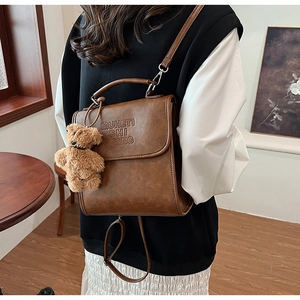 Dettaglio dello zaino vintage in pelle marrone con testo a rilievo e ciondolo a forma di orso