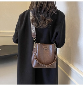 Detail of dark brown leather bucket bag with geometric jacquard wide strap and woven handle