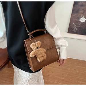Dettaglio borsa vintage in pelle PU marrone con scritte del marchio e ciondolo a orsetto