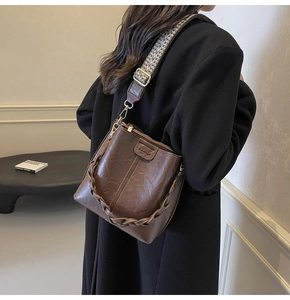 Detail of a brown leather bucket bag with an ethnic geometric woven wide strap