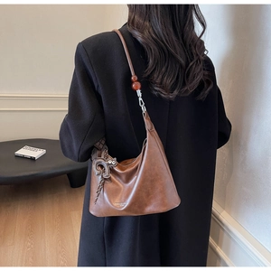 Close-up of brown leather hobo bag with cat charm and amber bead shoulder strap detail