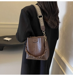 Brown leather bucket bag with geometric strap shown from a side back view on a model