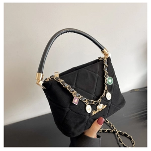 Detail of black quilted handbag with round handle and gold charms like 'Love You' pendant