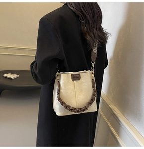 Detailed view of beige bucket bag with ethnic woven strap and logo patch on model