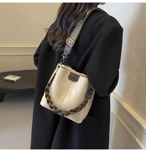 Detail of cream bucket bag with wide wavy strap and brown woven handle on model