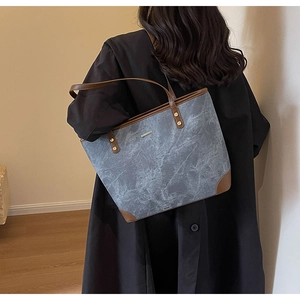 Detail of grey marble-patterned tote bag with brown leather straps worn on shoulder