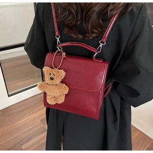 Vista dettagliata dello zaino in pelle bordeaux con testo sbalzato e ciondolo a orsetto