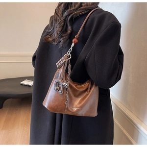 Brown leather hobo bag with chocolate charm and cat pendant worn as a stylish shoulder bag